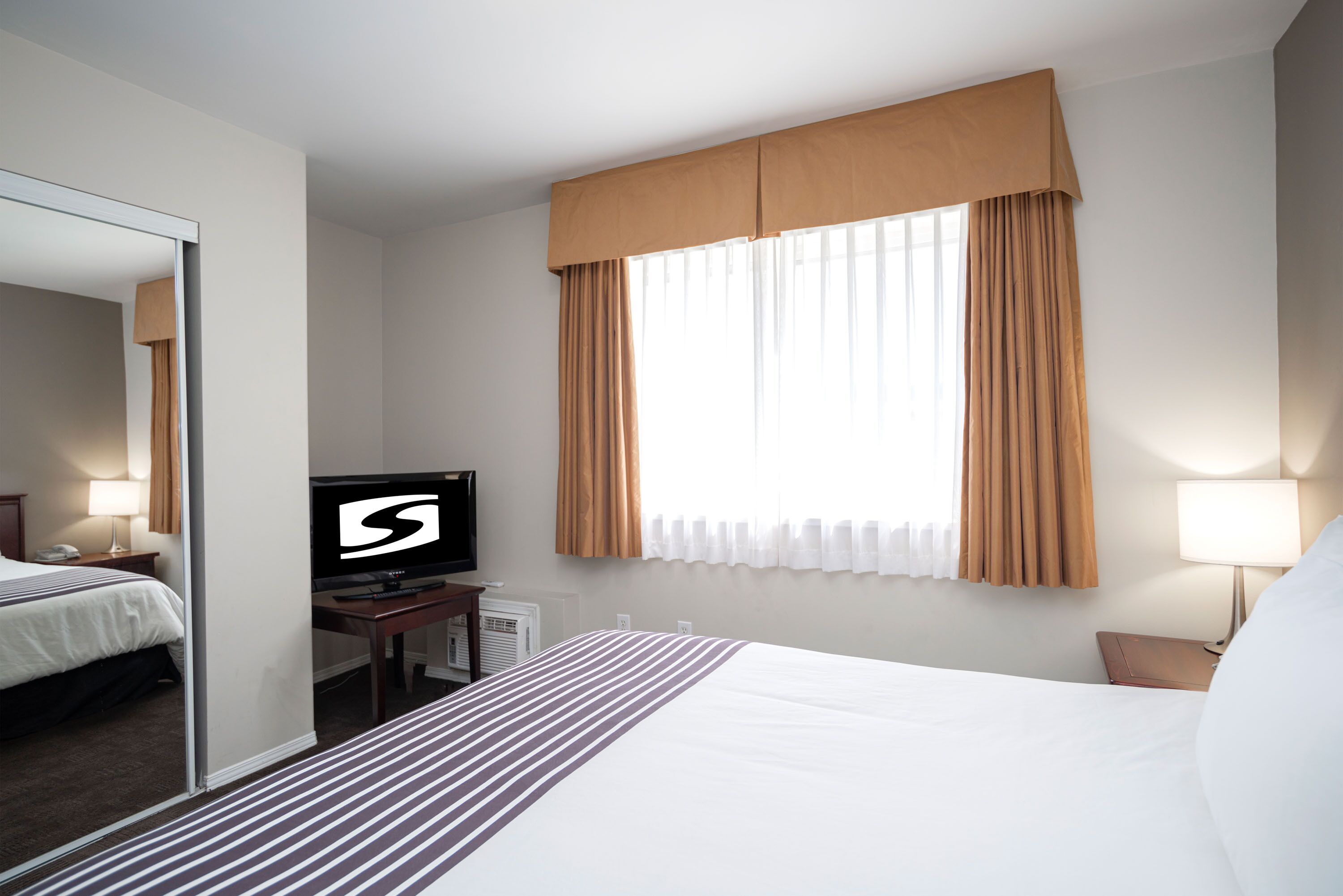 Una habitación de hotel con una cama grande, televisión, escritorio y ventana con cortinas.