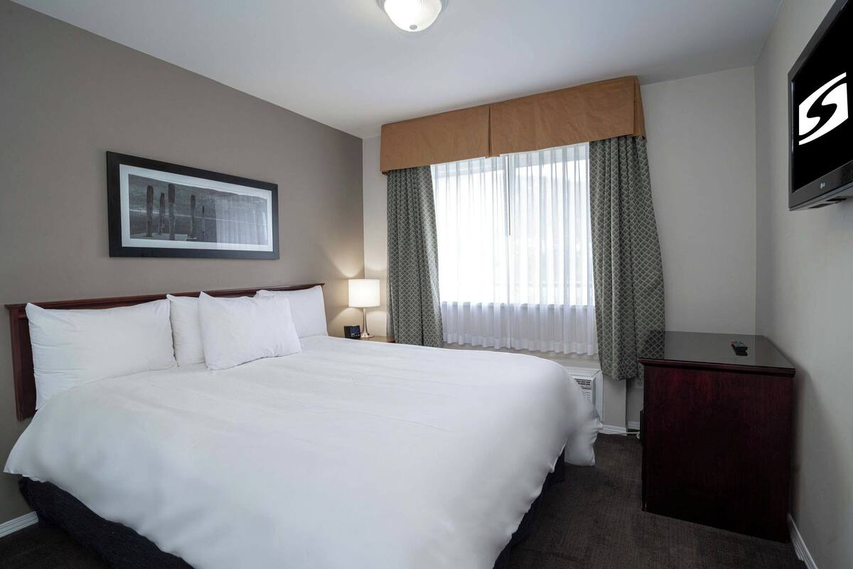 Een hotelkamer met een groot bed, een nachtkastje, een televisie en een raam met gordijnen.
