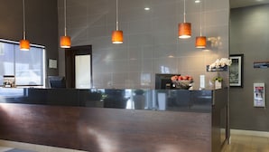 Un comptoir d’accueil avec un revêtement en bois foncé, des suspensions orange et une petite plante posée sur le comptoir.
