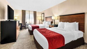 A hotel room with two beds, a desk, a TV, and a window with curtains.