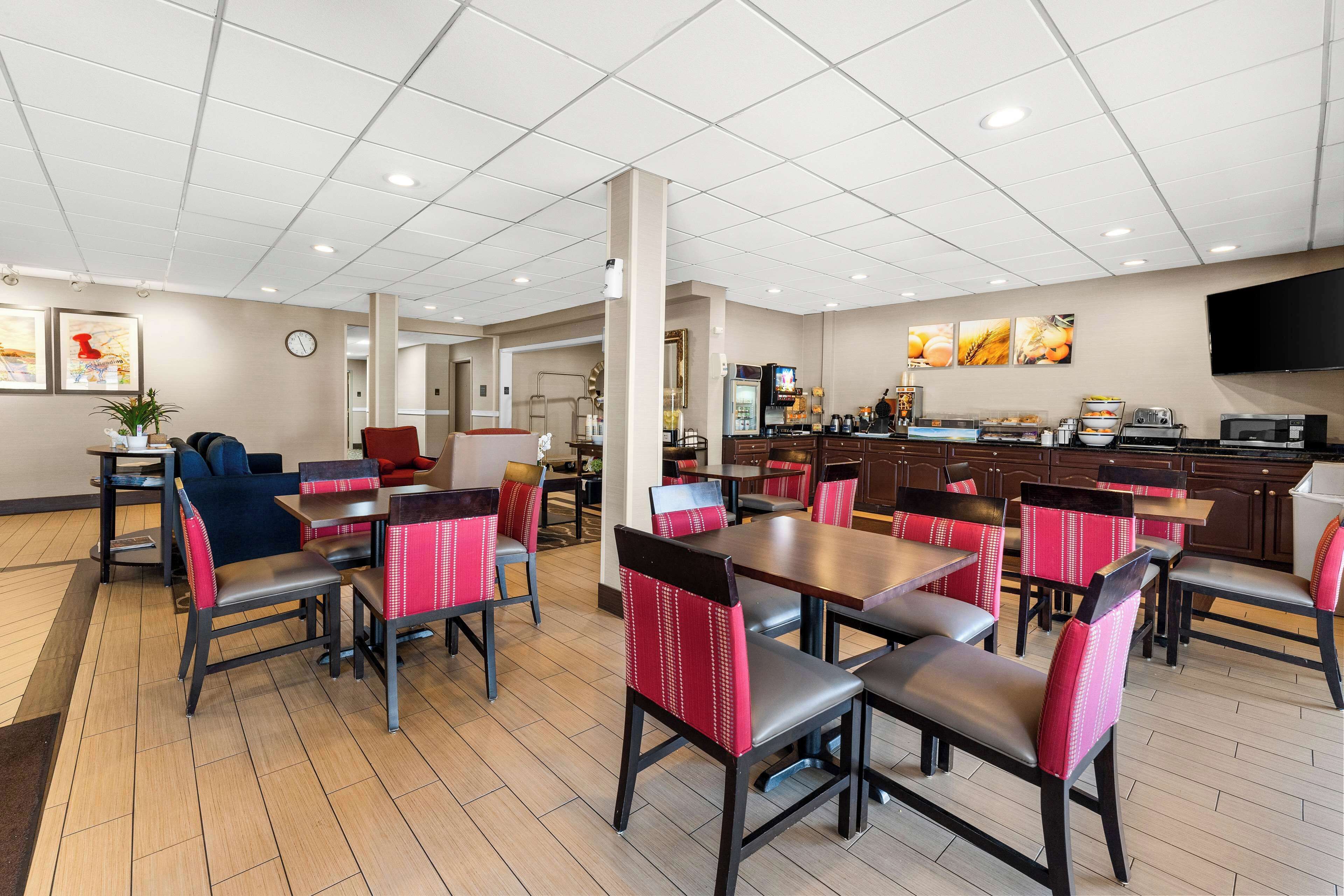 Un grand espace dédié à la salle à manger, avec plusieurs tables et chaises, un coin cuisine équipé d’appareils électroménagers et une horloge au mur.