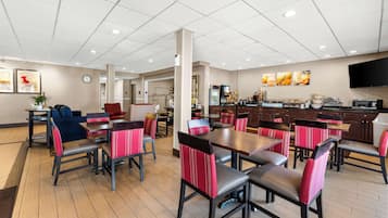 Un grand espace dédié à la salle à manger, avec plusieurs tables et chaises, un coin cuisine équipé d’appareils électroménagers et une horloge au mur.