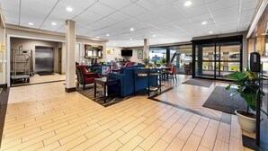 A spacious lobby with a wooden floor, seating area with sofas and chairs, a reception desk, and a large window offering a view outside.