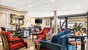 A hotel lobby with a sofa, armchairs, a coffee table, a TV, and a kitchen area.