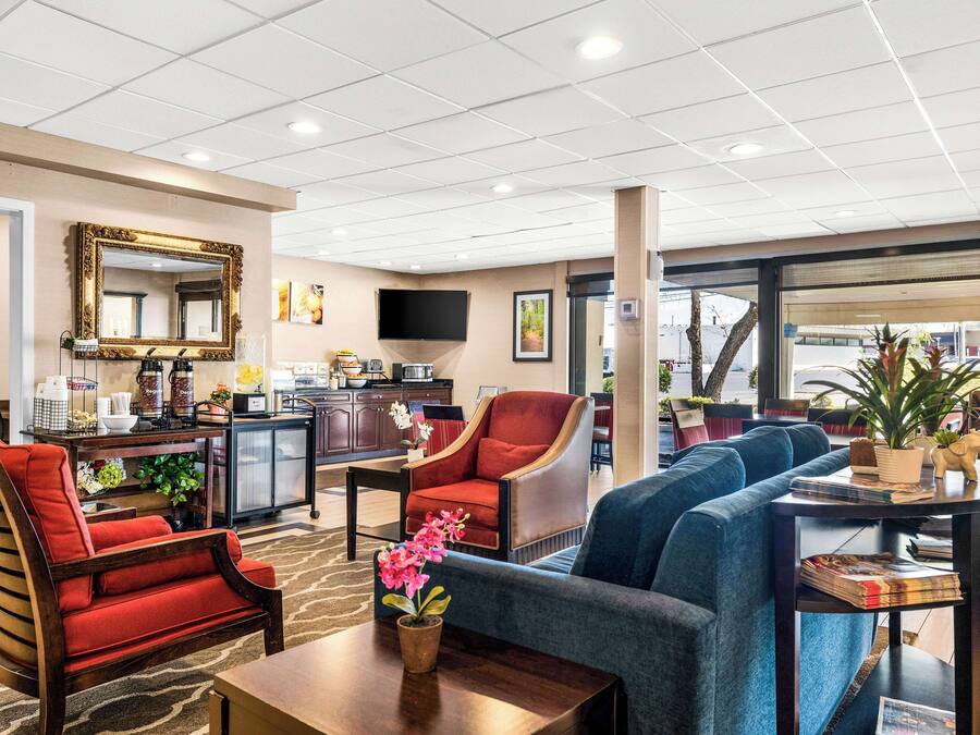 A hotel lobby with a sofa, armchairs, a coffee table, a TV, and a kitchen area.