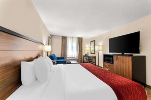A hotel room with a large bed, a desk, a chair, a television, and a wardrobe.