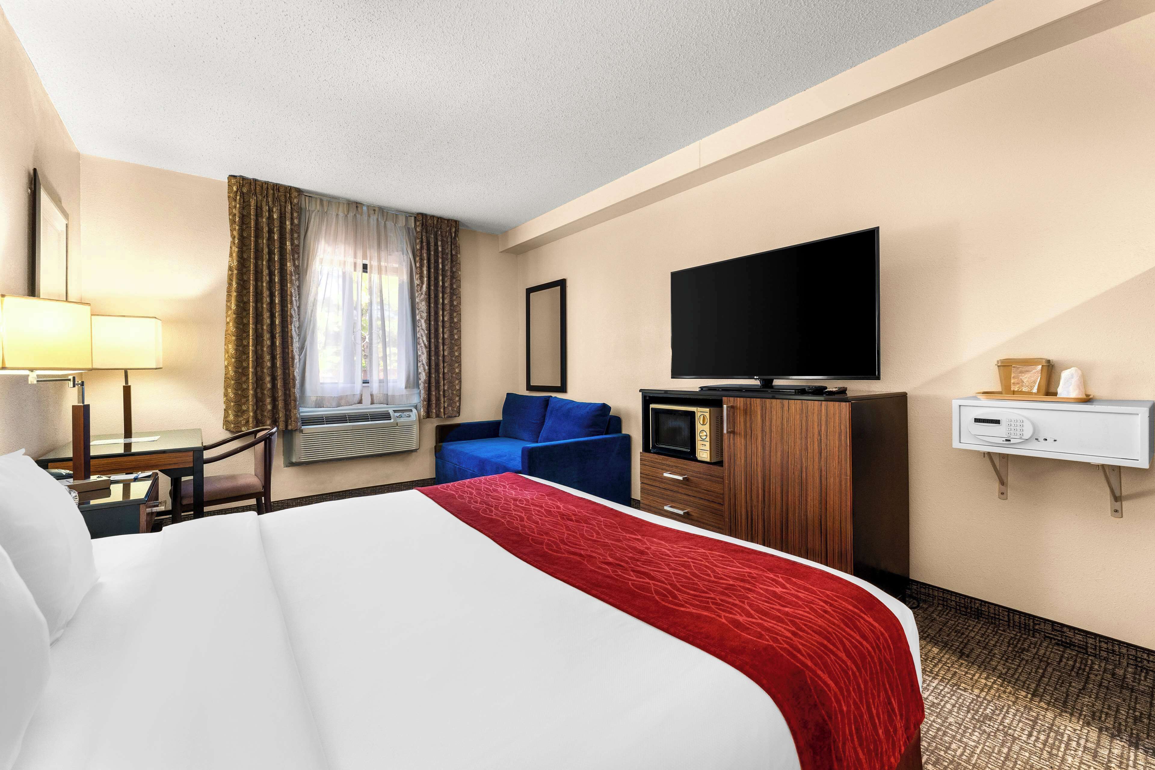 A hotel room with a large bed, a desk with a lamp, a television, and a minibar.