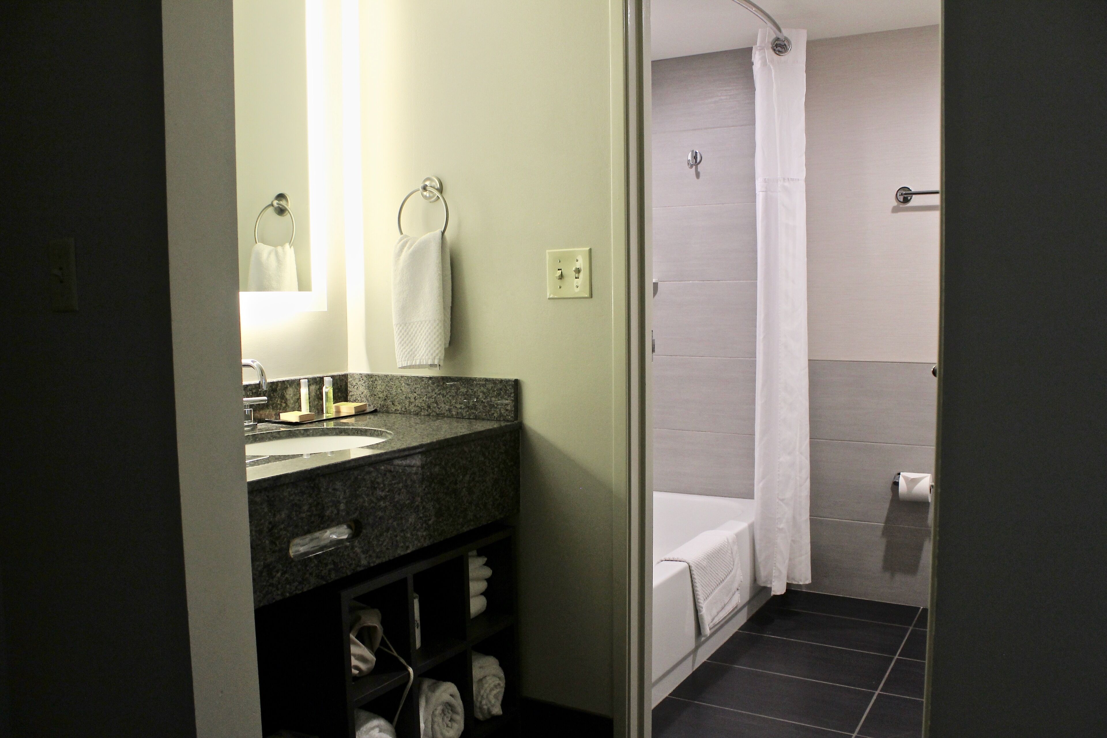 A bathroom with a granite countertop sink, a mirror, a towel rack, a shower with a curtain, and a toilet.