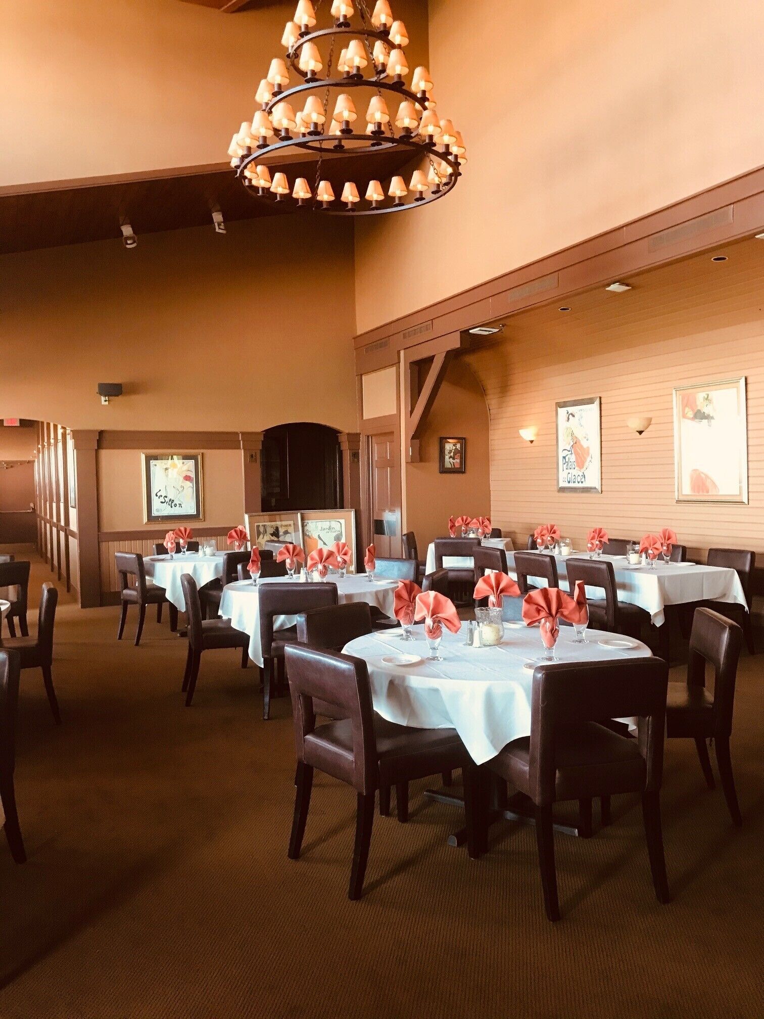 A restaurant with multiple tables set for dining, featuring white tablecloths and red napkin rings.
