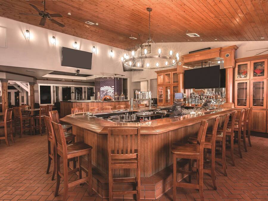 A spacious bar area with wooden bar stools, a large wooden bar counter, and a ceiling fan.
