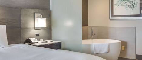 Ein Hotelzimmer mit Bett, Nachttisch, Telefon und einem Badezimmer mit Badewanne und Toilette.