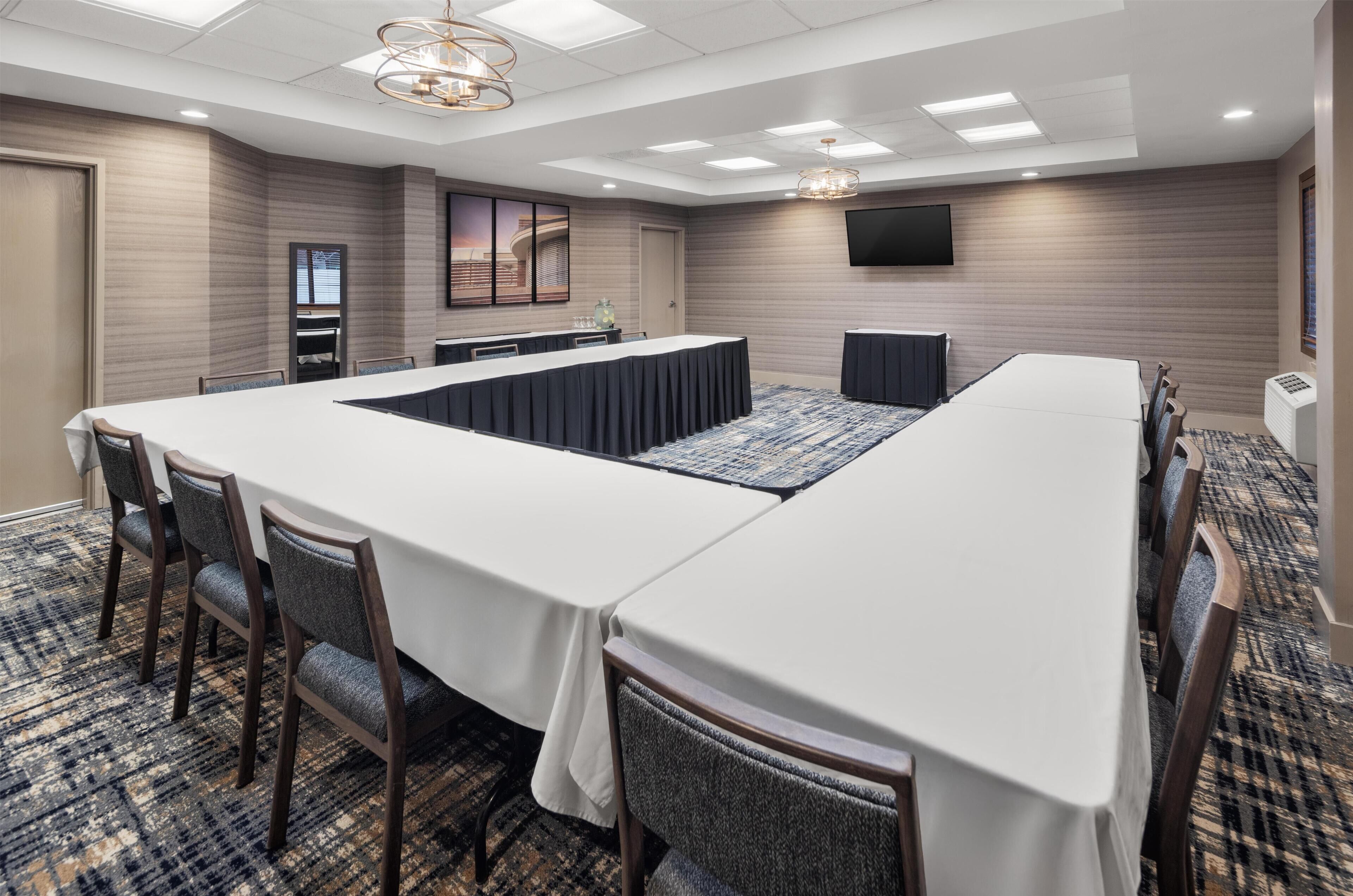 A conference room with a long table, chairs, a flat-screen TV, and a carpeted floor.