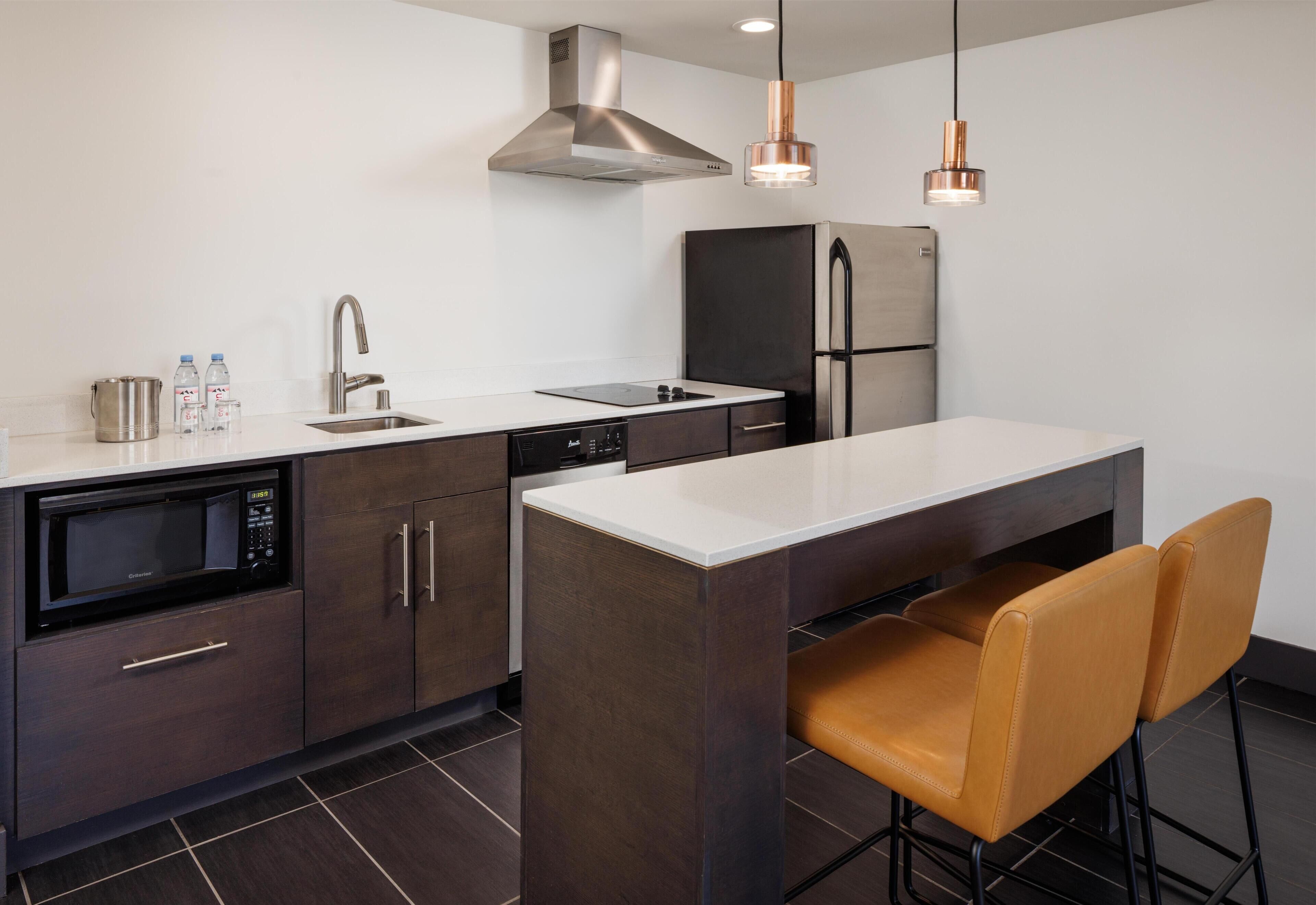 Een moderne keuken met een ingebouwde magnetron, roestvrijstalen apparatuur en een centraal eiland met barkrukken.