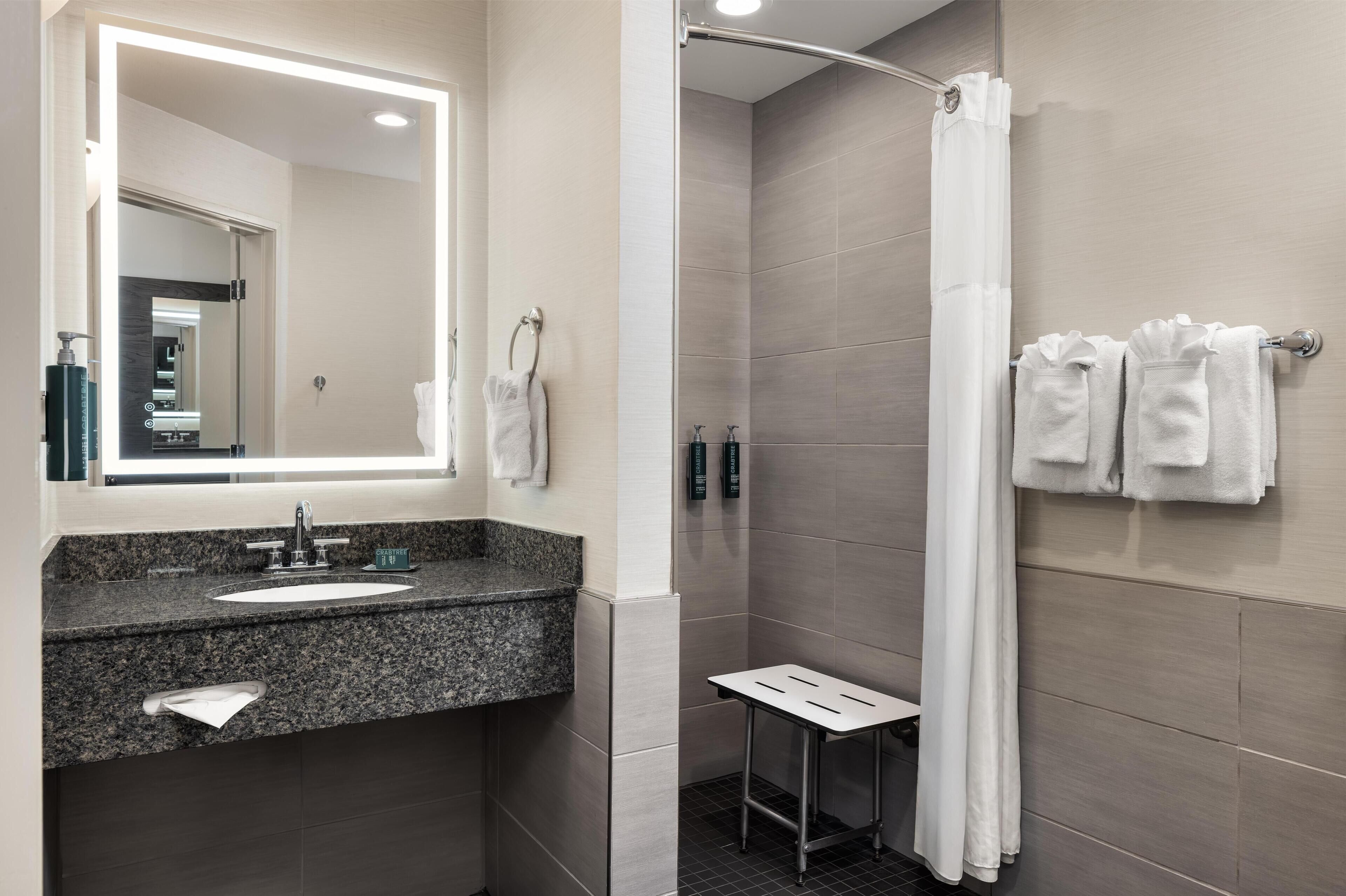 A bathroom with a sink, mirror, towel rack, shower curtain, and a small table.