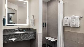 A bathroom with a sink, mirror, towel rack, shower curtain, and a small table.