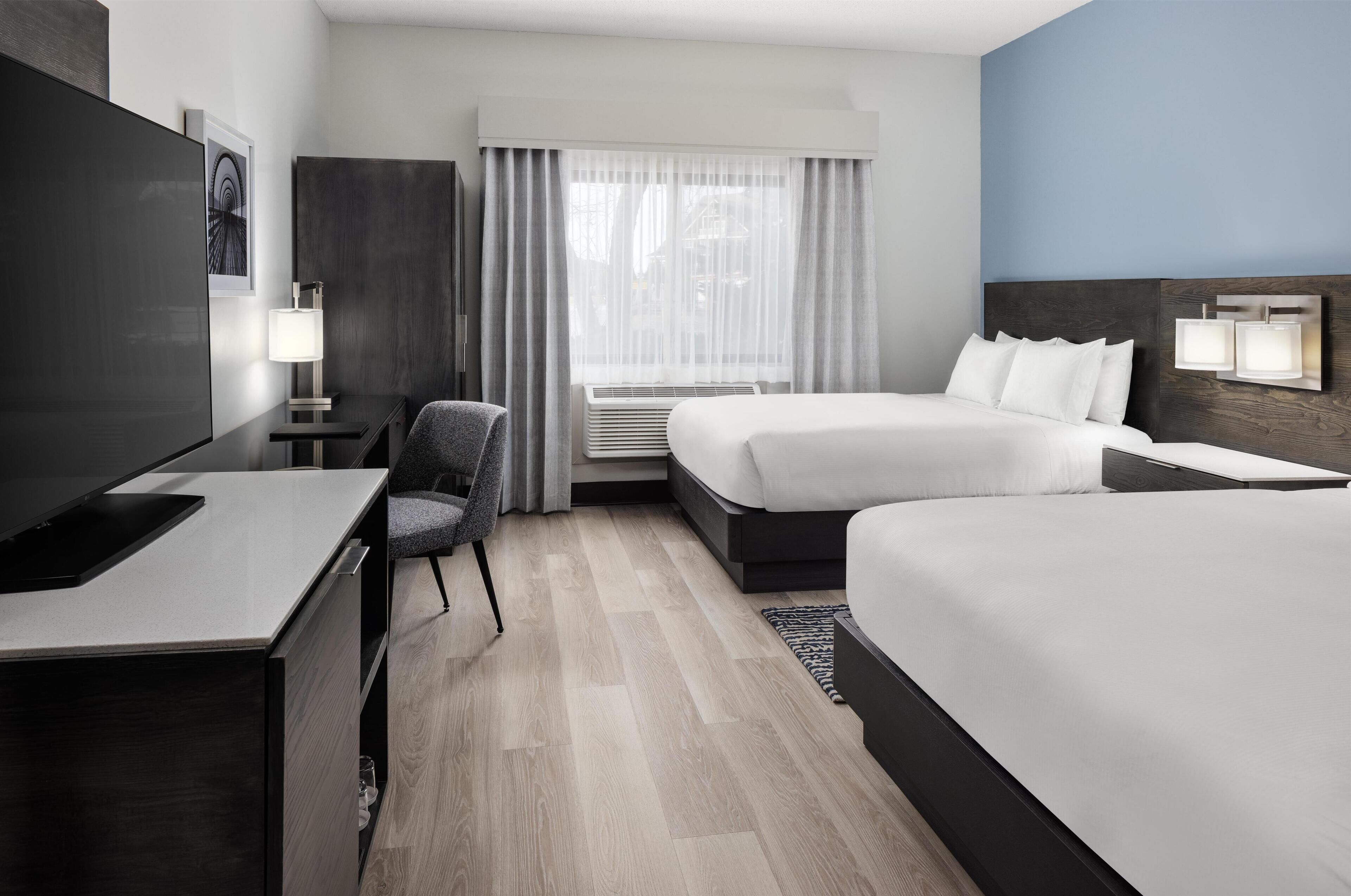 Een hotelkamer met een bed, een bureau, een stoel, een televisie en een raam met gordijnen.