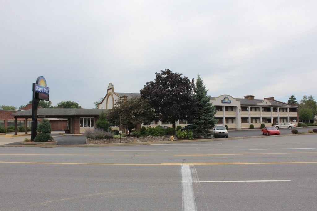 A Days Inn with a parking lot, a large tree, and a building with a distinctive arched entrance.