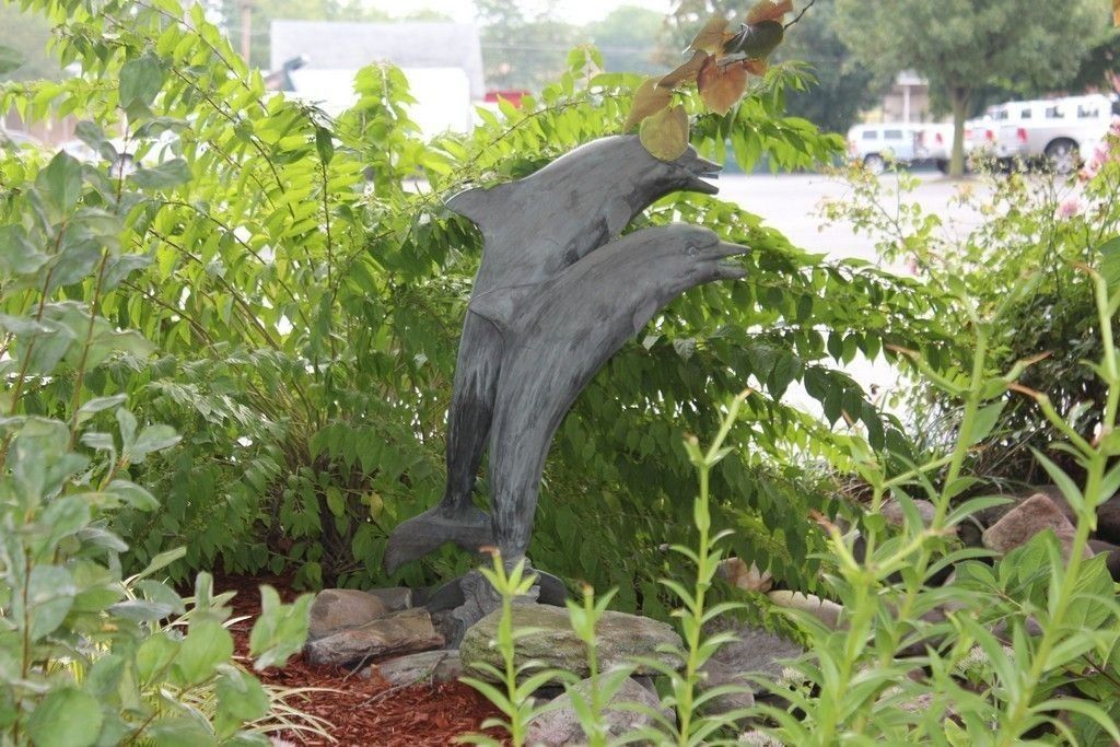 A garden with a sculpture of dolphins amidst lush greenery and rocks.