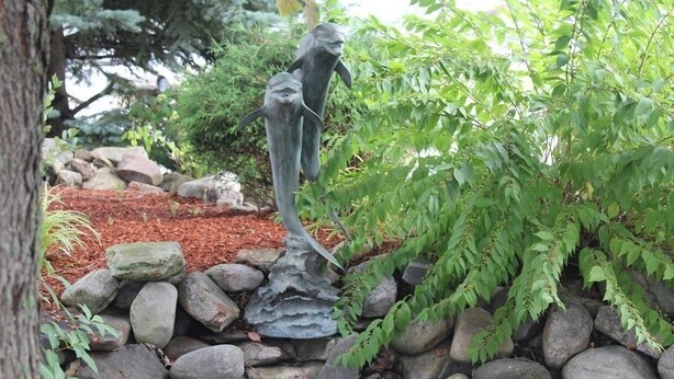Un jardín con una estatua de delfín, rodeado de rocas y follaje.