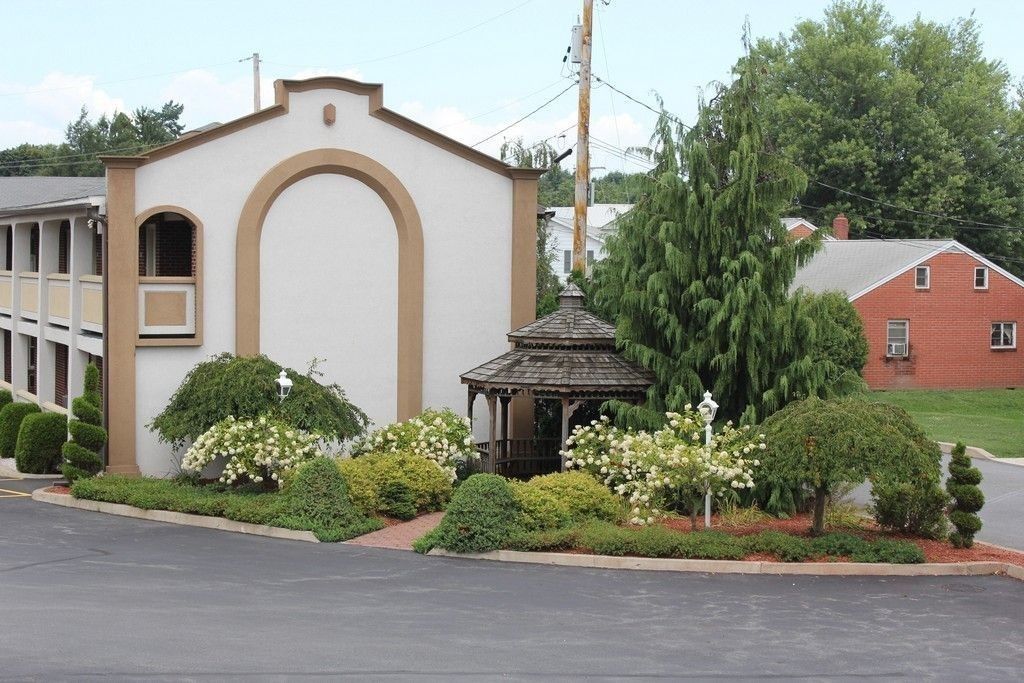 Un edificio con fachada blanca y arco marrón, rodeado de jardines cuidados y un pabellón.