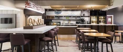 A modern bar area with a long counter, multiple stools, and a variety of bar tools and bottles.