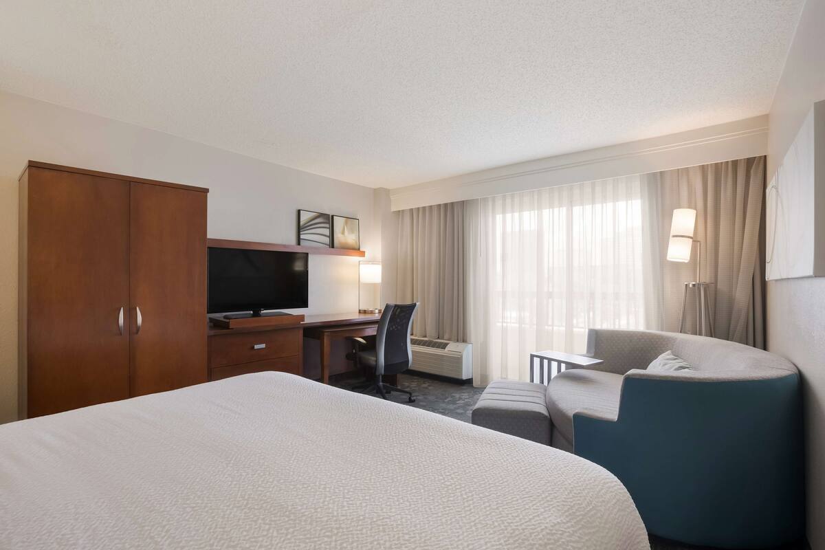 A hotel room with a large bed, a desk with a chair, a television, a lamp, and a sofa.