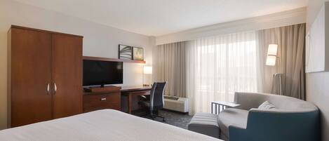 Habitación de hotel con una cama grande, un escritorio con silla, televisor, lámpara y sofá.