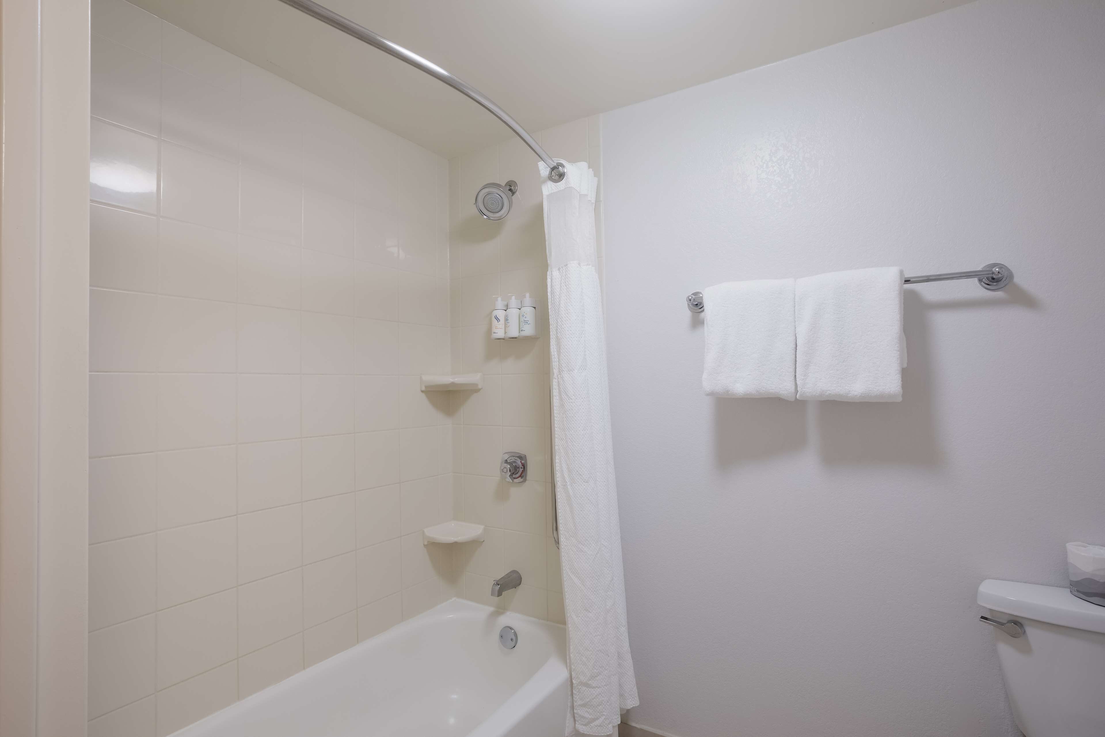 A bathroom with a bathtub, a shower curtain, a towel rack with two towels, and a toilet.