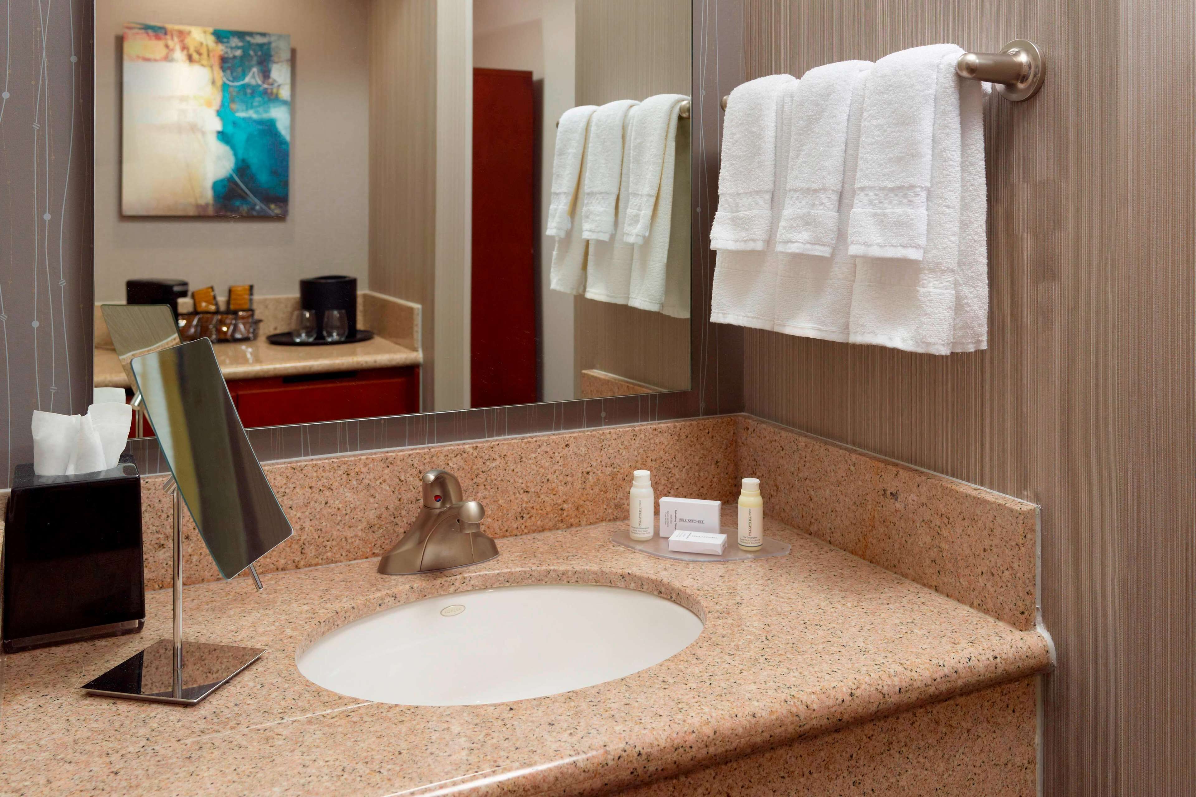 A bathroom with a granite countertop, a sink, a mirror, and a towel rack with white towels.