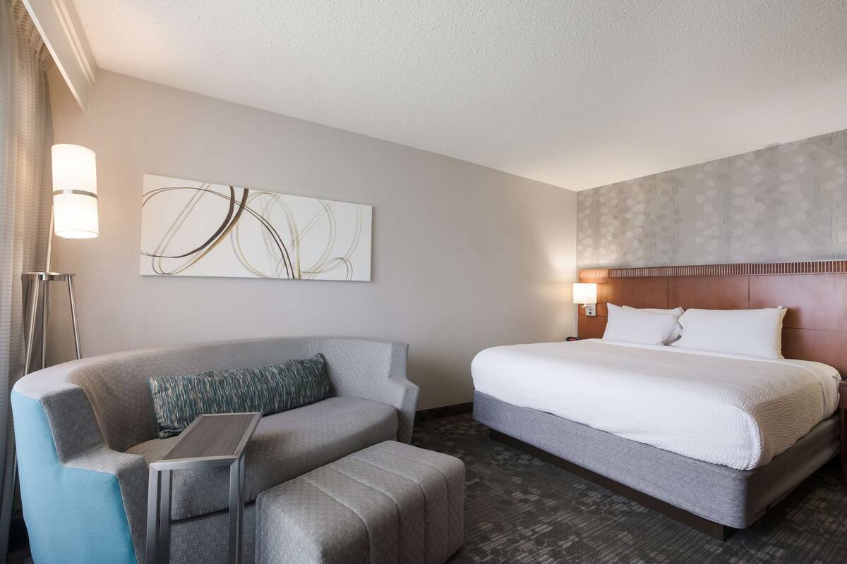 A hotel room with a bed, a sofa, a small table, and a wall-mounted artwork.