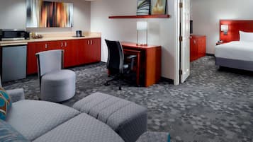 A hotel room with a kitchenette, a desk with a chair, a bed, and a seating area with ottomans.