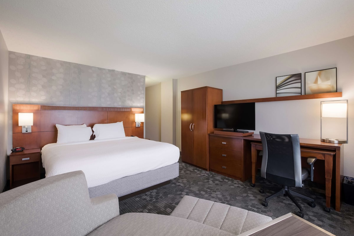 A hotel room with a large bed, a desk with a chair, a television, and a wardrobe.