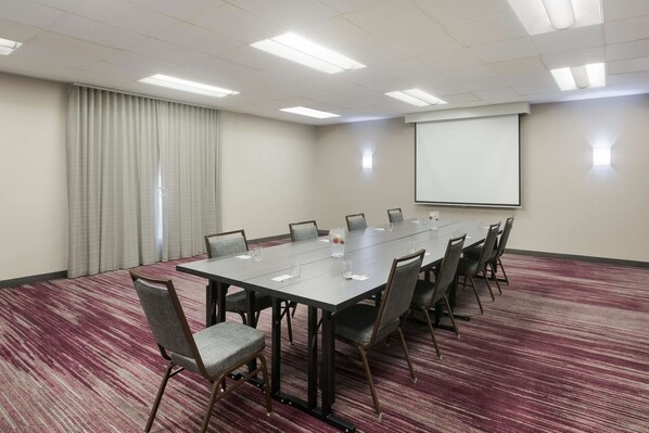 A conference room with a long table, chairs, a projector screen, and a carpeted floor.