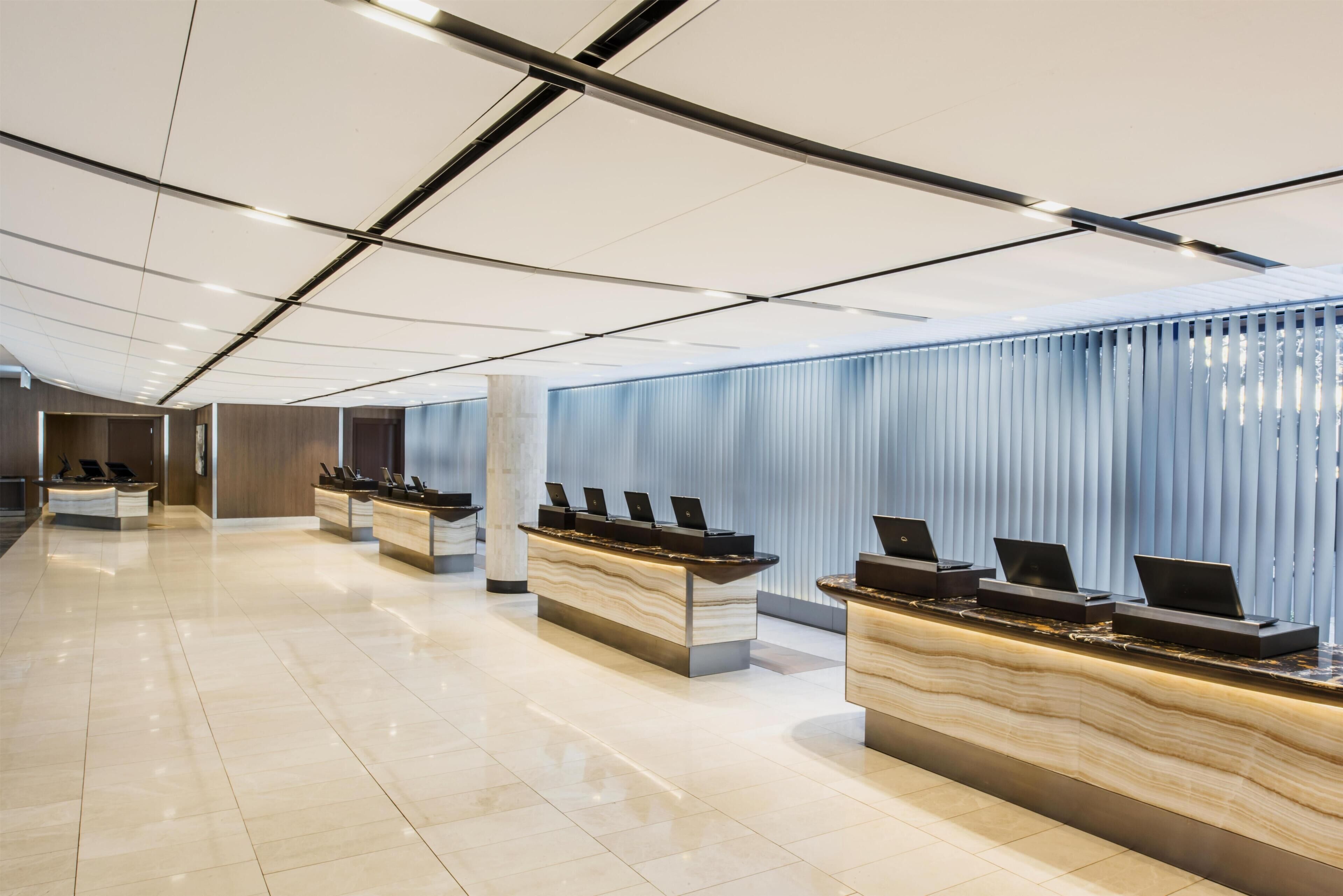 A modern hotel reception area with multiple counters, a polished floor, and a ceiling with linear lighting.