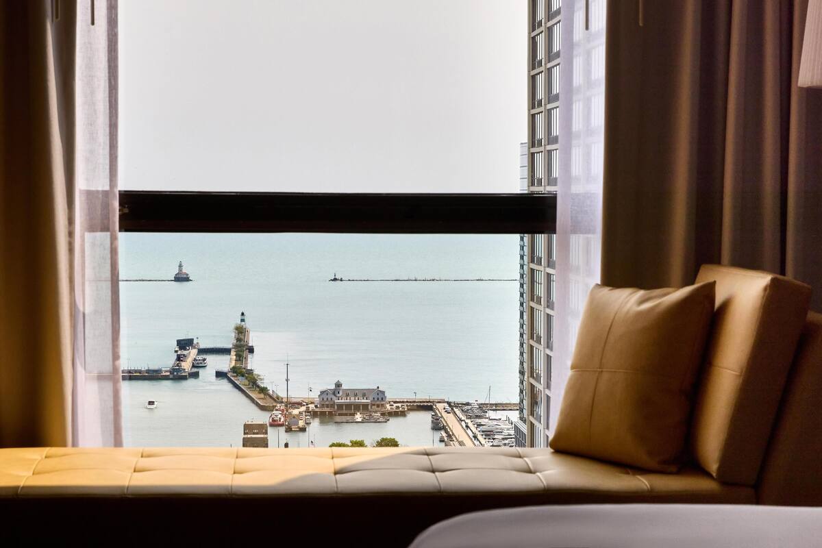 A hotel room with a view of a marina, a building with a lighthouse, and a distant pier.
