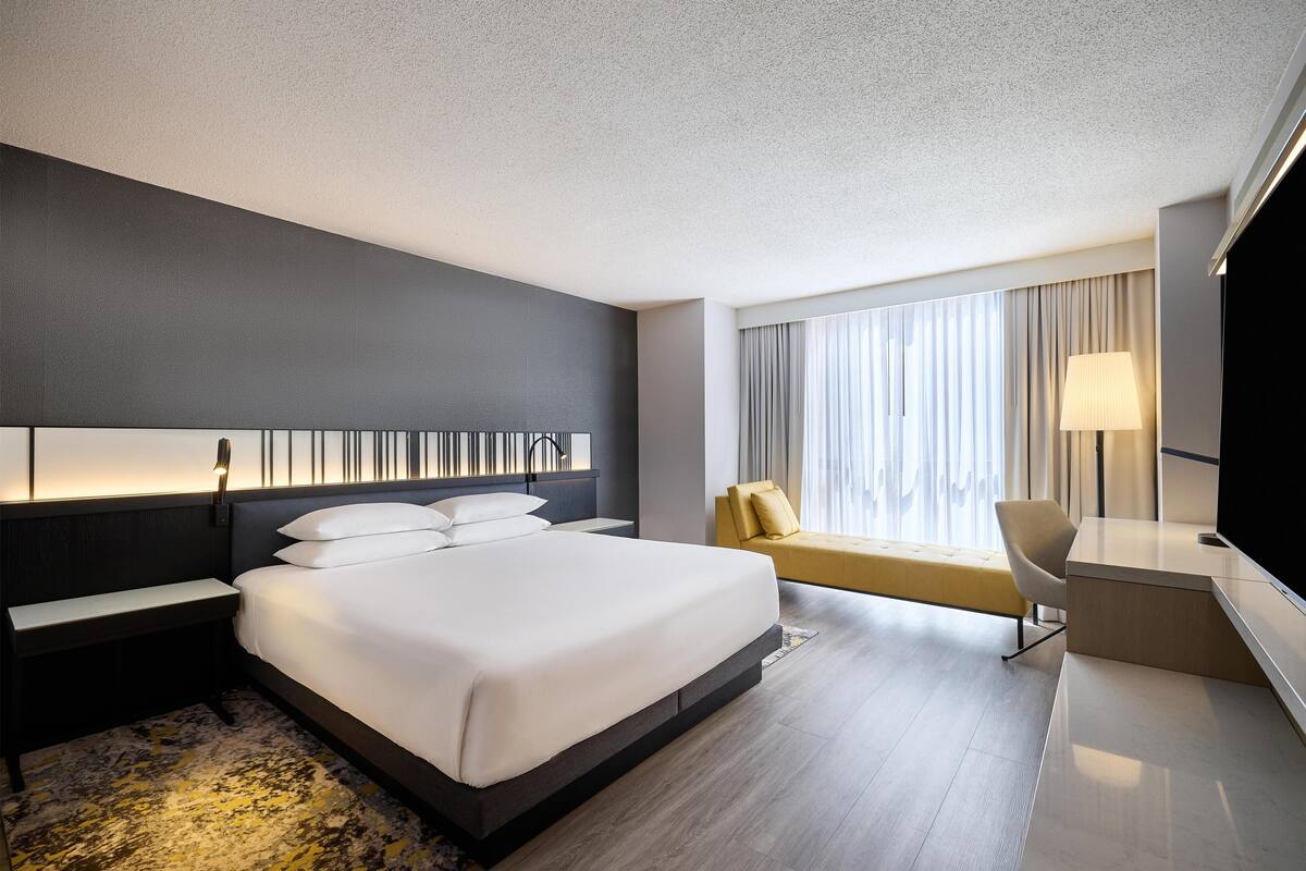 A modern hotel room with a large bed, bedside tables, a desk, a chair, and a TV.