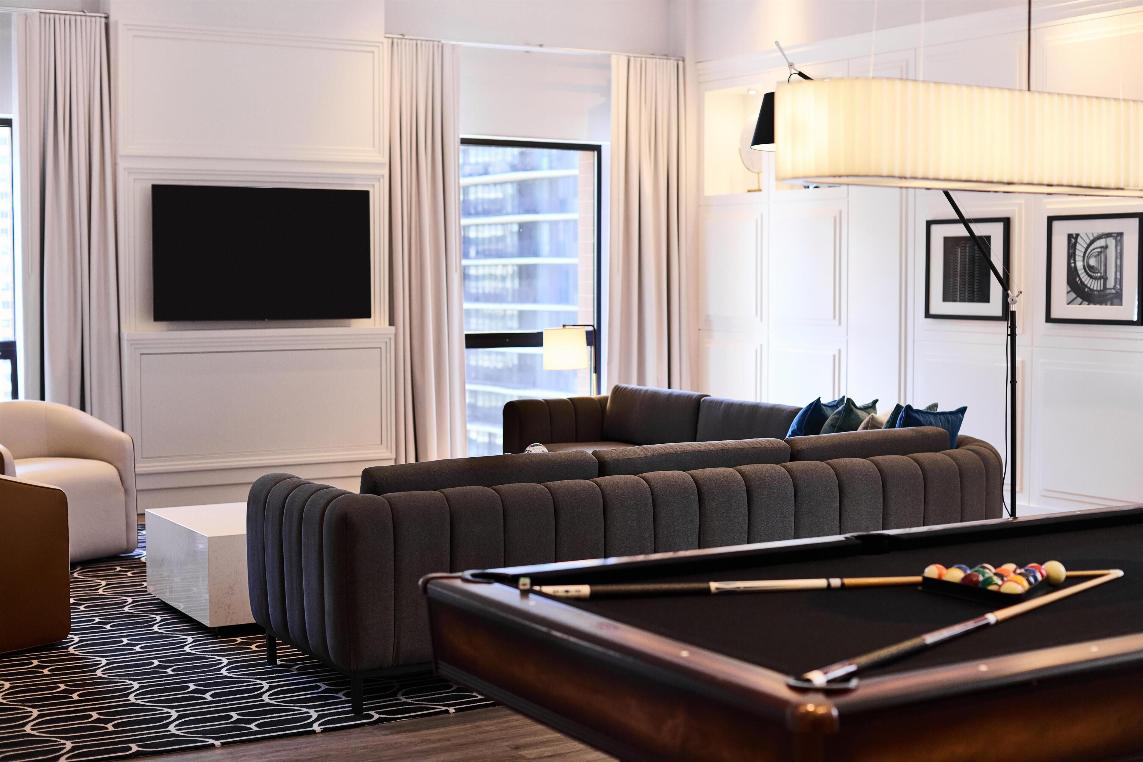 A modern living room with a pool table, a sofa, a television, and a large window.