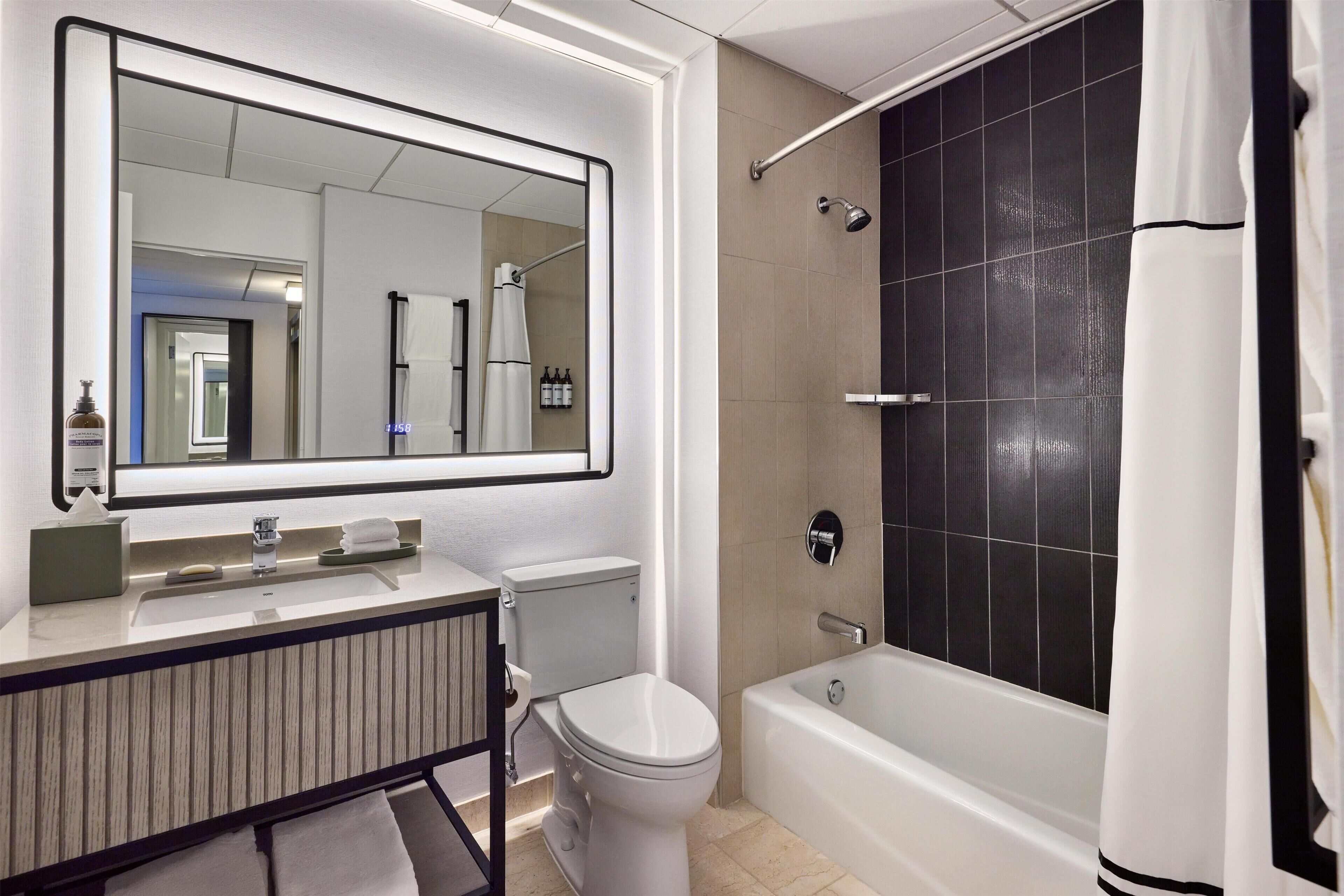A modern bathroom with a large mirror, a toilet, a sink, and a bathtub.