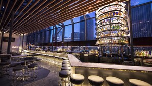 A bar with a circular liquor display, seating with stools, and a city view through large windows.