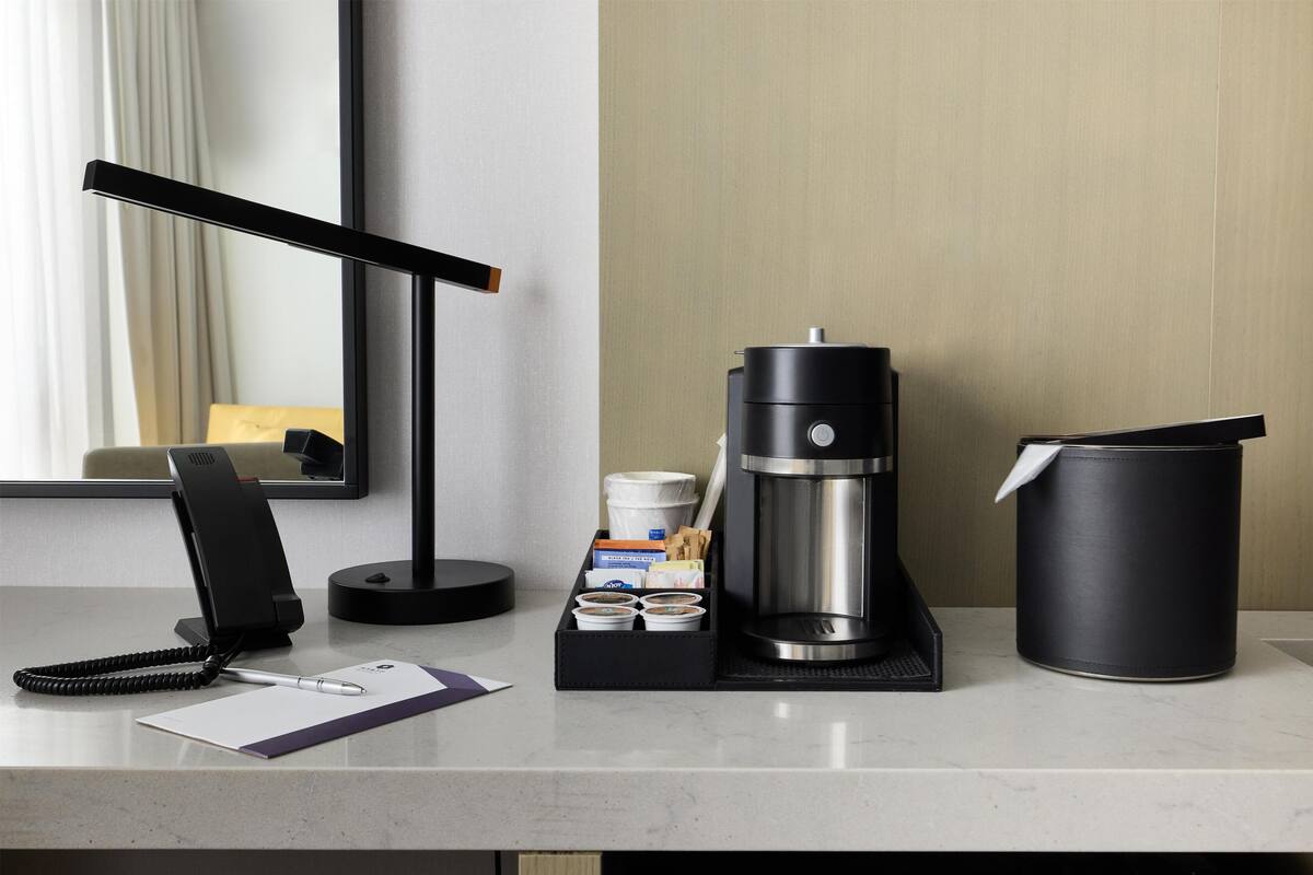 A hotel desk with a coffee maker, a phone, a notepad, and a tray with cups and a tissue.