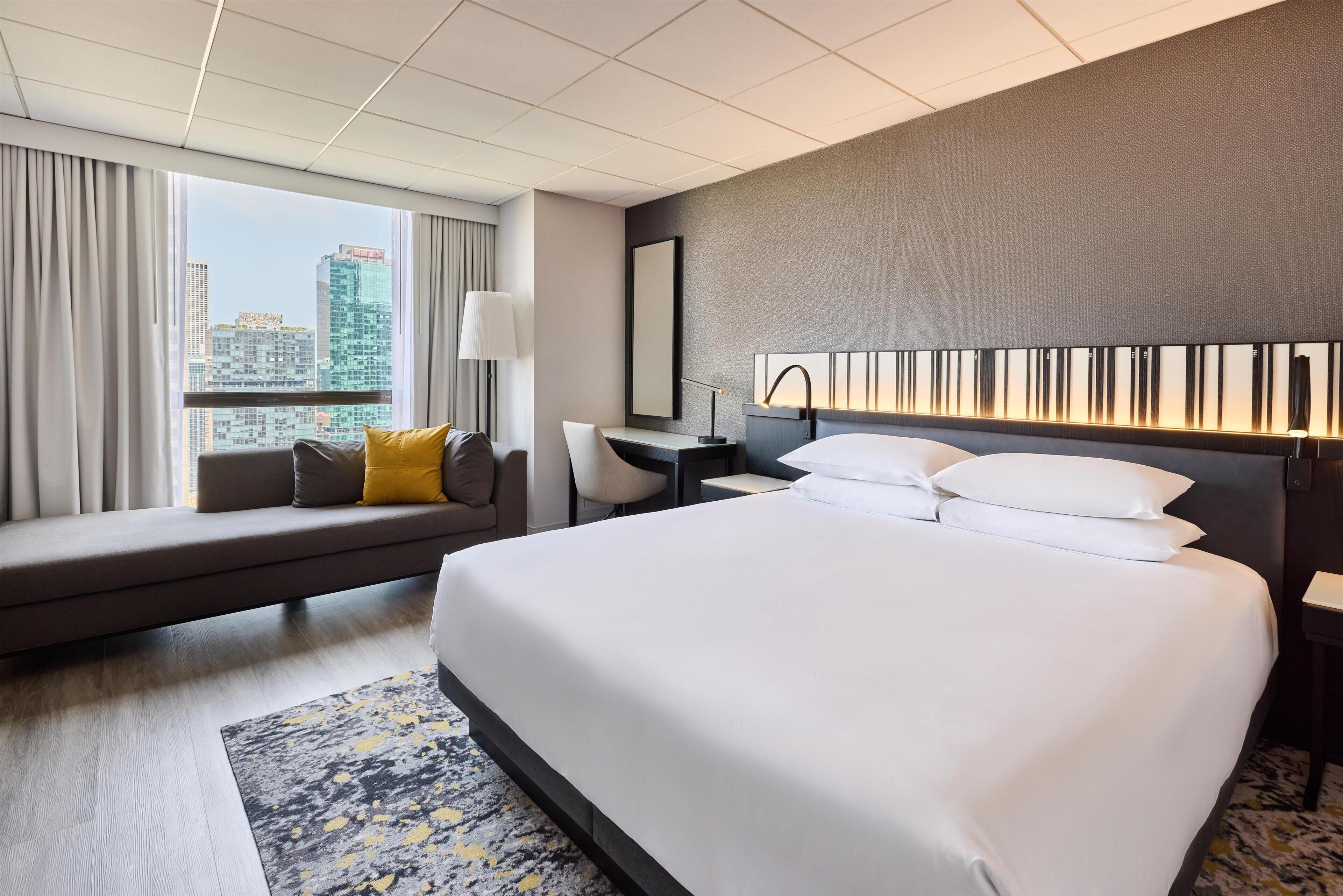 Habitación de hotel con una cama grande, un sofá, un escritorio y vistas a la ciudad.