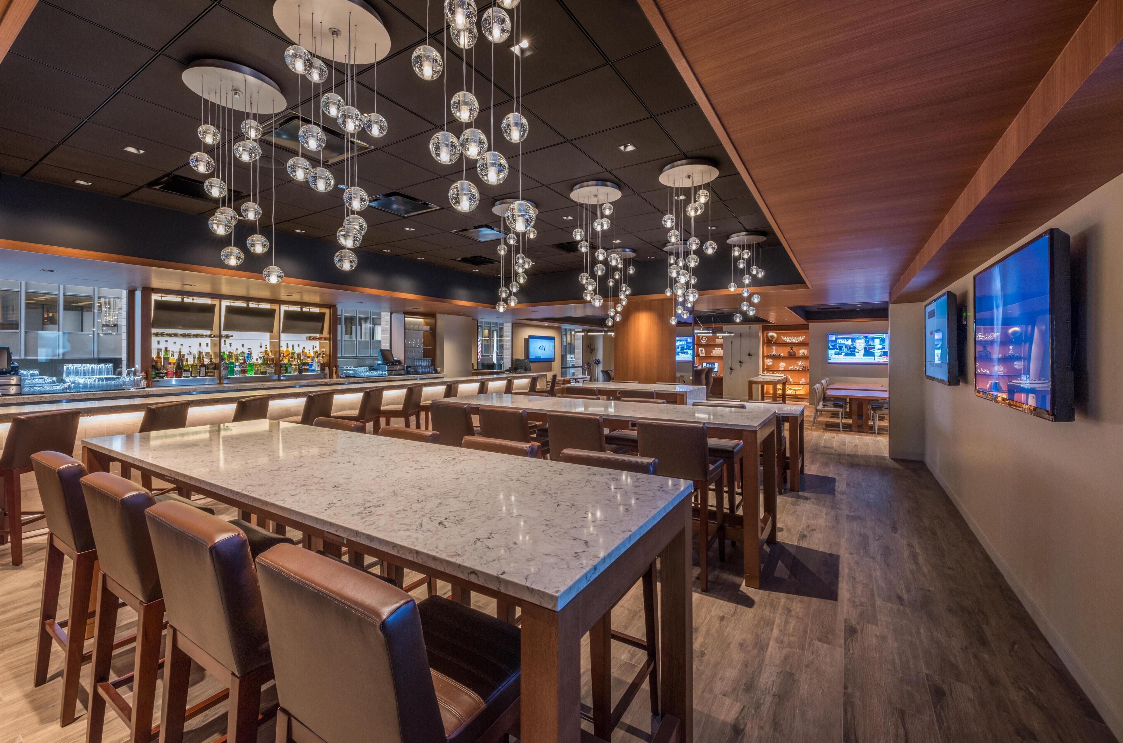 A bar area with multiple seating tables, hanging spherical light fixtures, and a television screen.