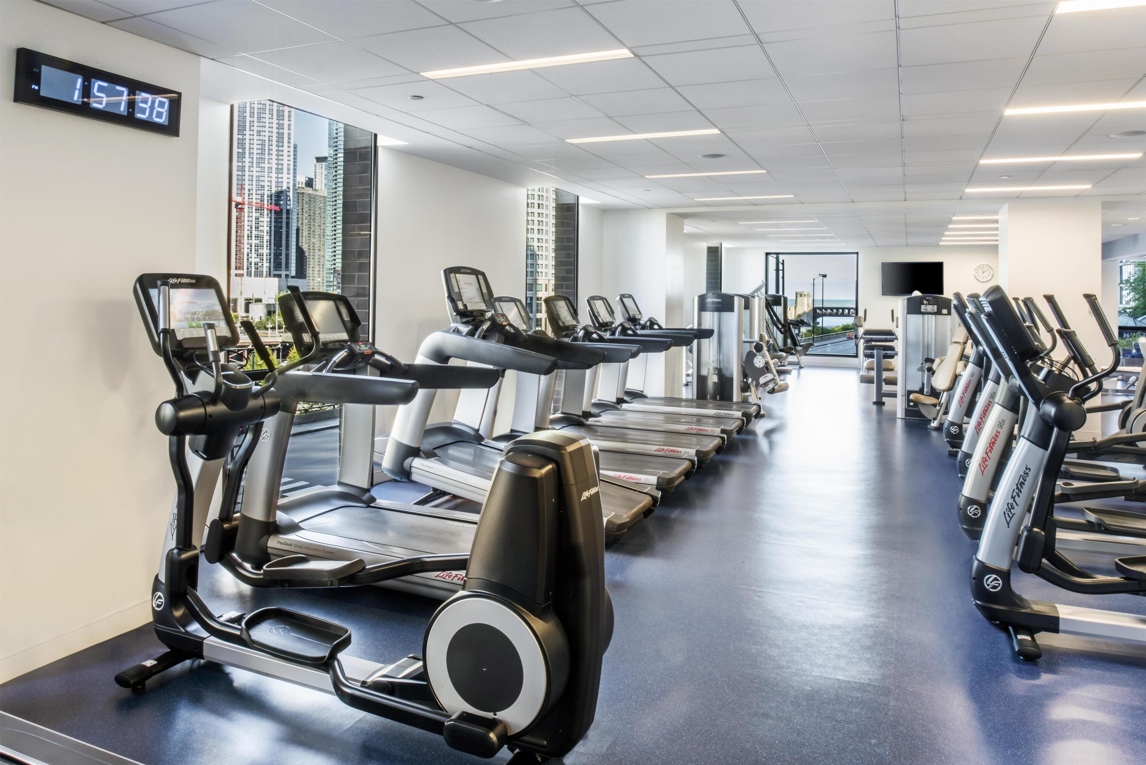 A gym with treadmills, ellipticals, and a digital clock displaying 1:57:38.