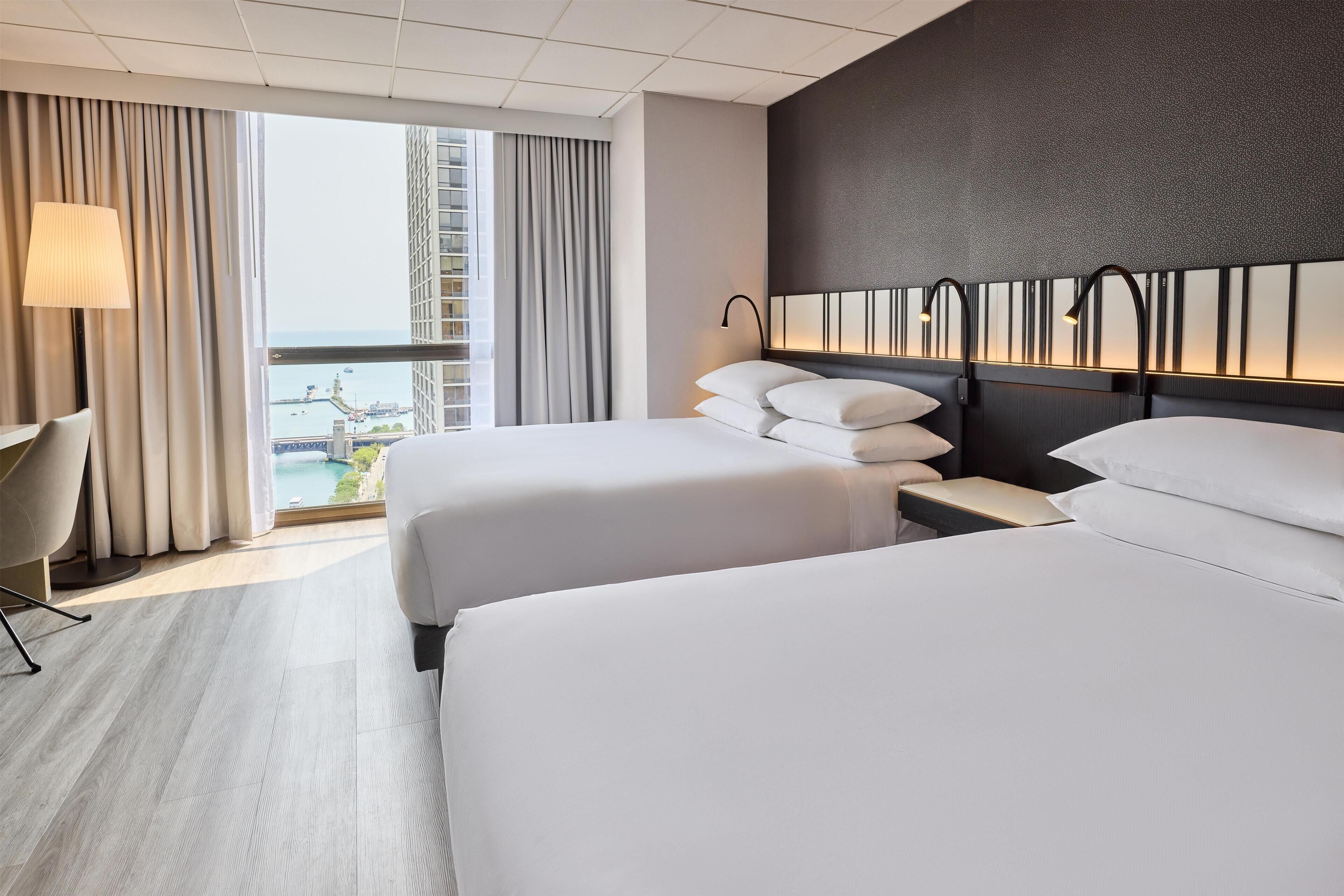 A hotel room with two beds, a view of the city, and a modern design.