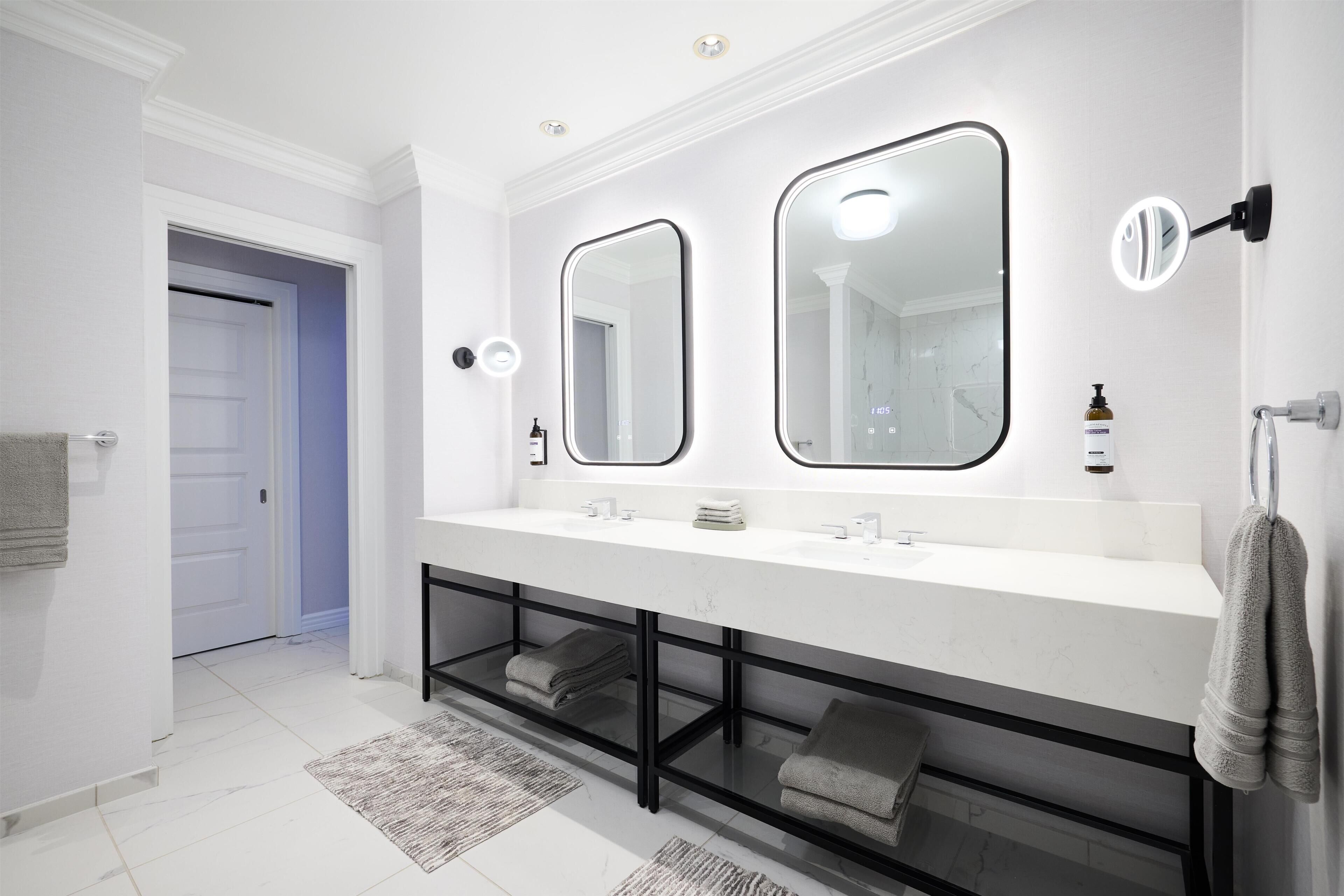 A modern bathroom with a double vanity, two mirrors, a towel rack, and a built-in shelf.