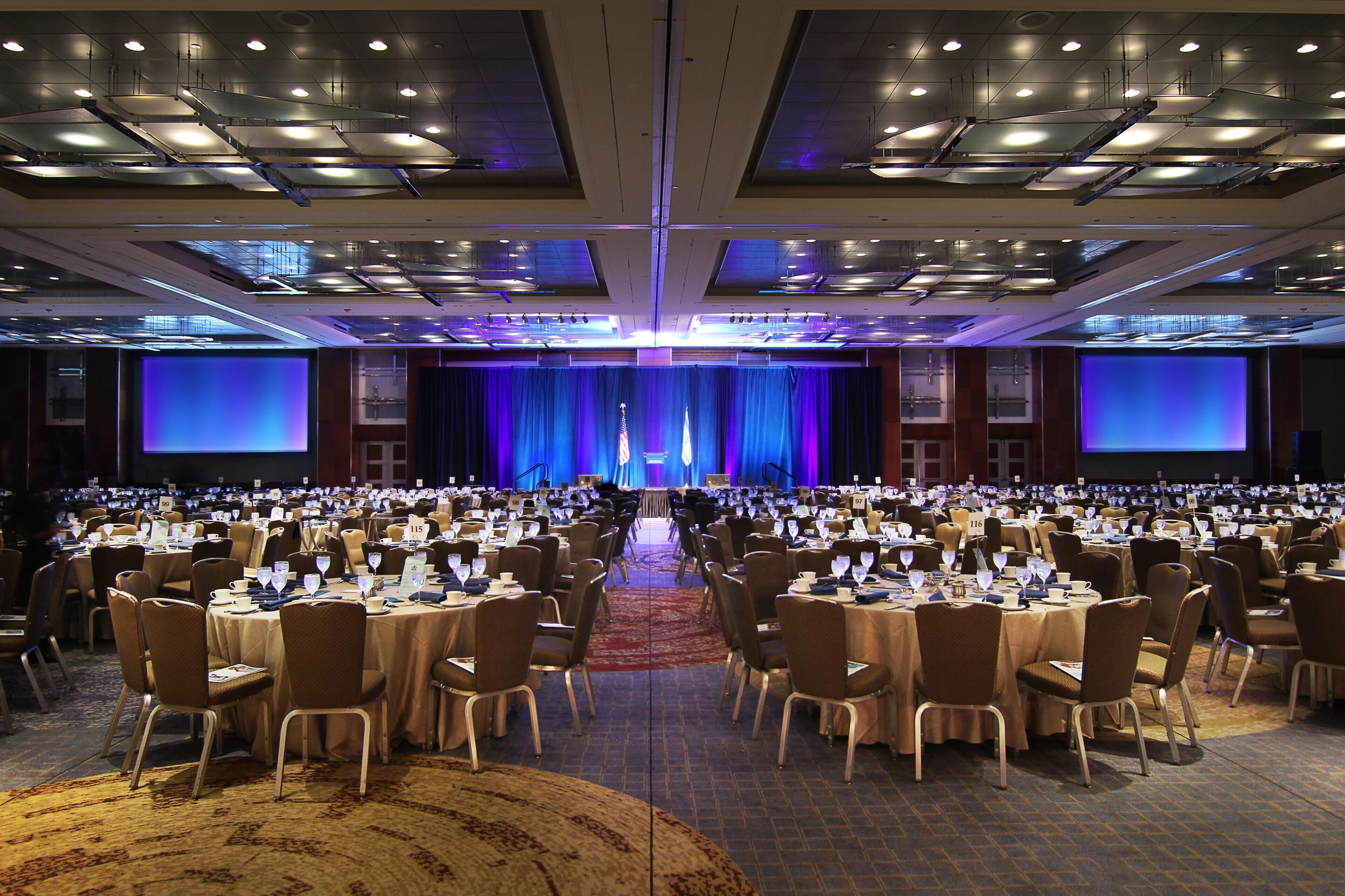 A large conference room with rows of tables and chairs, a stage with a blue curtain, and a podium.