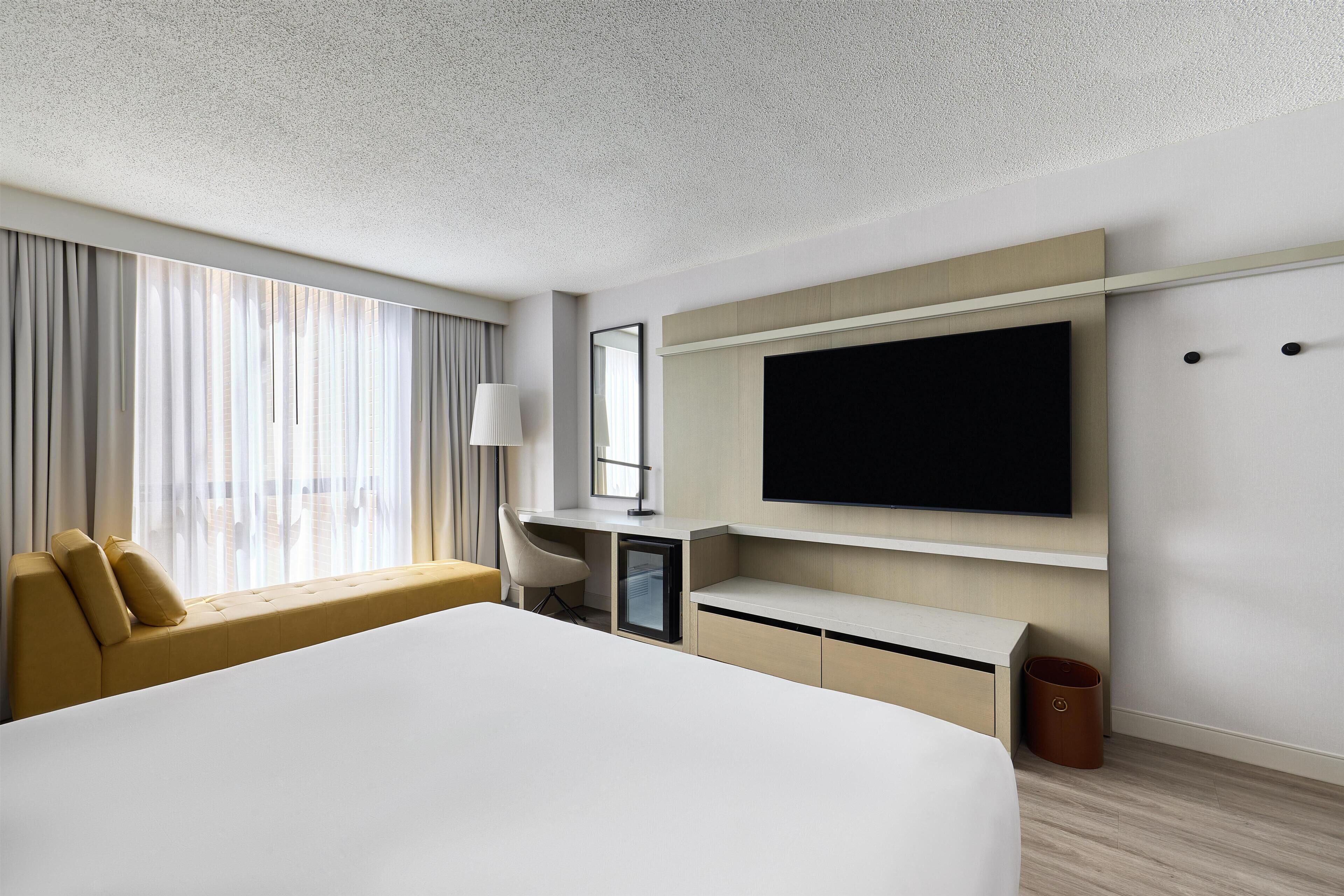 A modern hotel room with a large bed, a desk, a television, and a window with curtains.