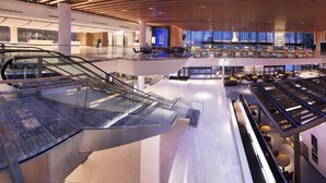 A multi-level hotel lobby with a glass elevator, a seating area, and a dining space.