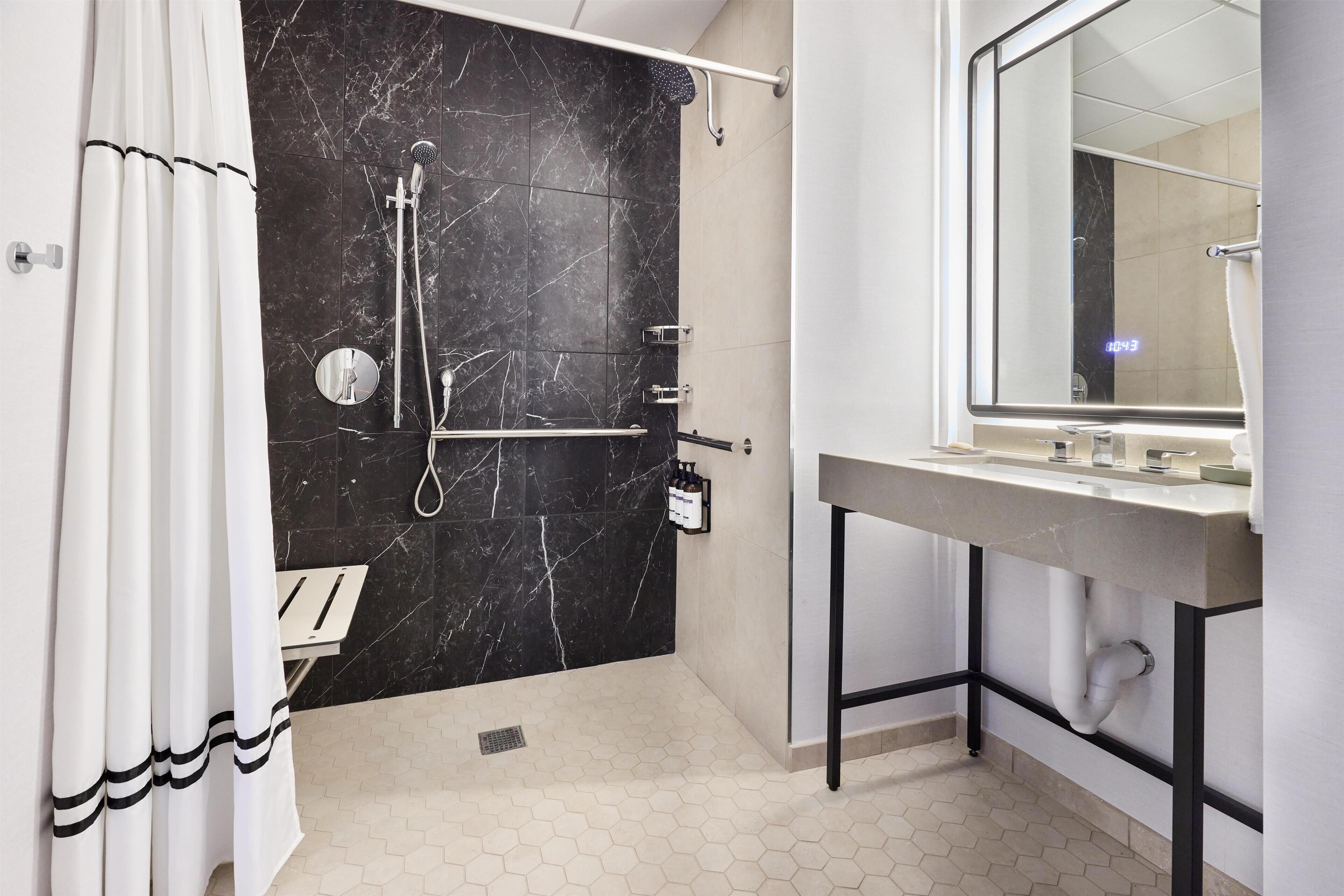 A modern bathroom with a black marble shower wall, a white sink with a mirror, and a white tiled floor.
