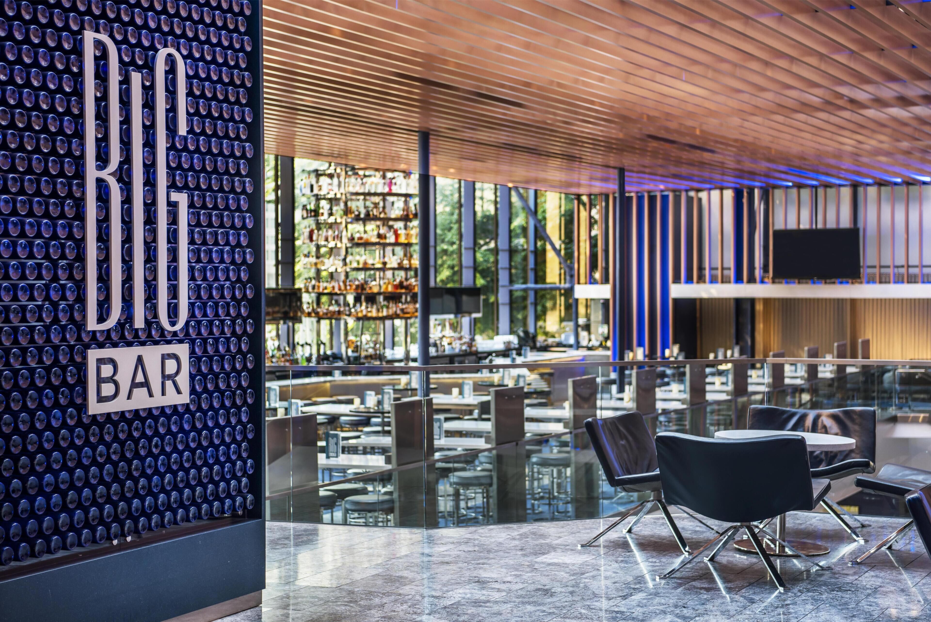 A modern bar with a unique glass wall design, a wooden ceiling, and a view of the outdoor seating area.